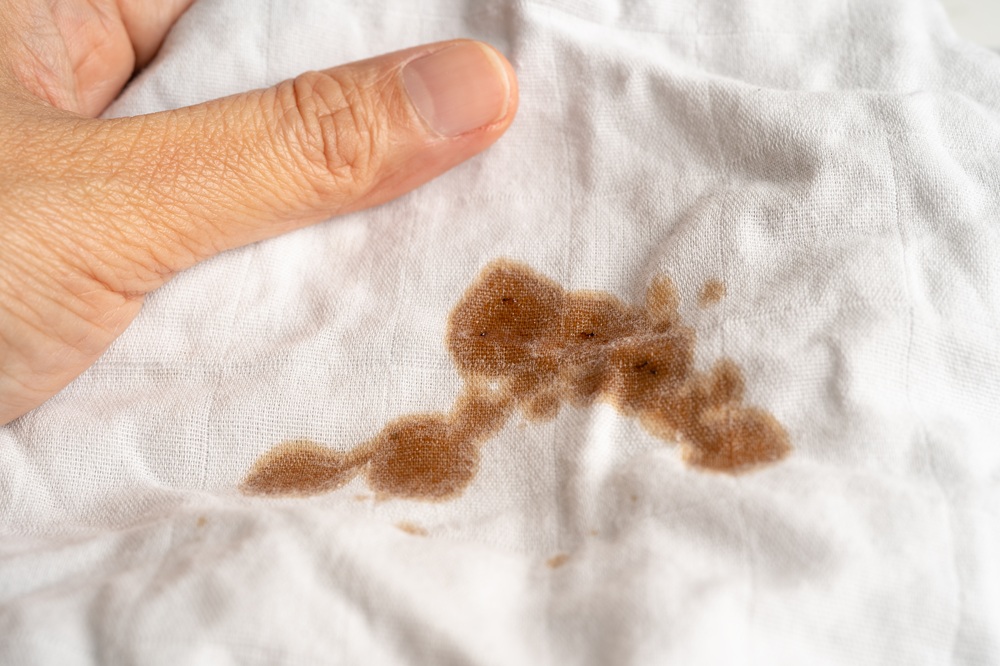 A hand holding white fabric stained with a brown liquid.