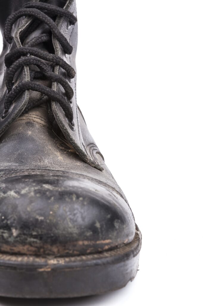 A close-up of a worn black leather boot with visible creases and scuff marks, photographed against a white background.