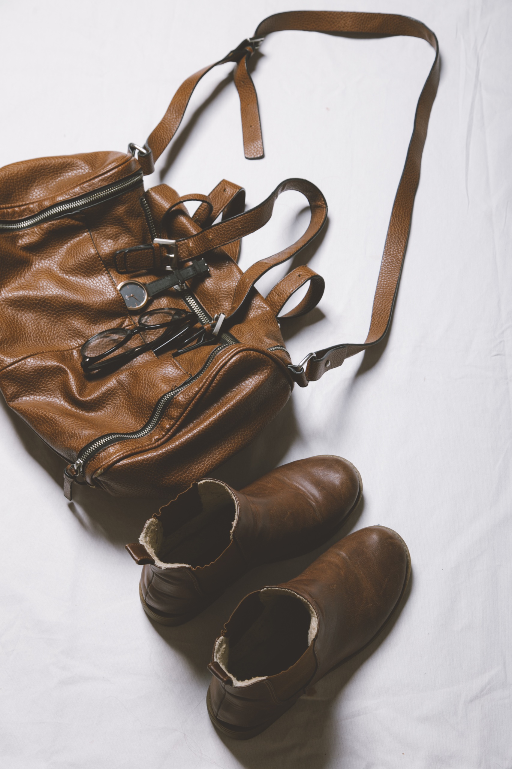 A brown leather bag with matching brown ankle boots is placed on a white surface.