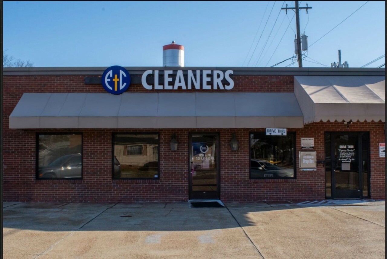 A brick building with a sign reading "Cleaners" above the entrance; windows and doors are visible on the storefront.