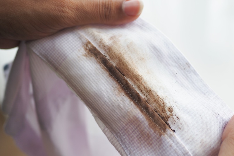 A close-up of hands holding a white shirt collar stained with dirt or grime.